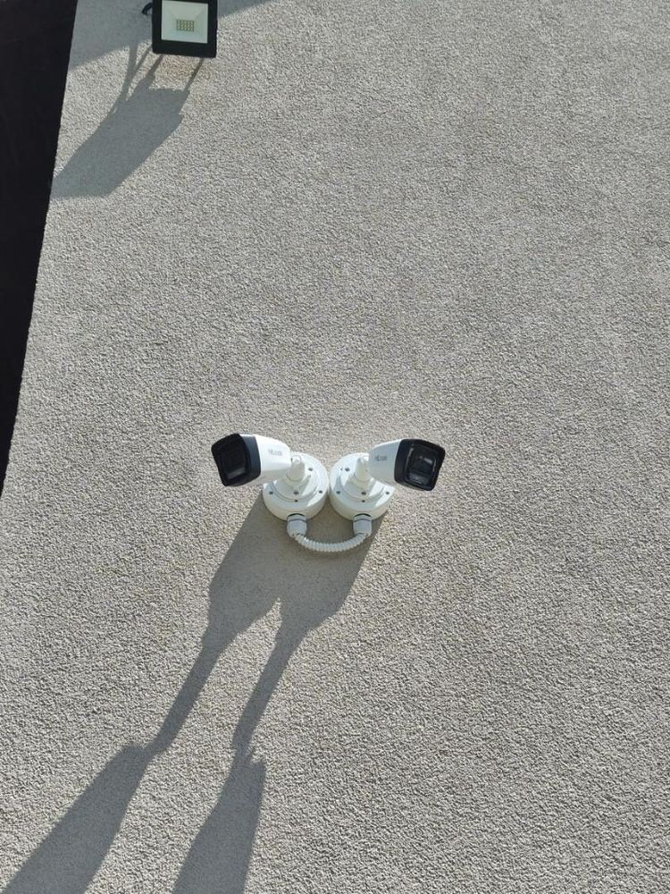 Dvije kamere na spojenim nosačima na fasadi, ispod reflektora